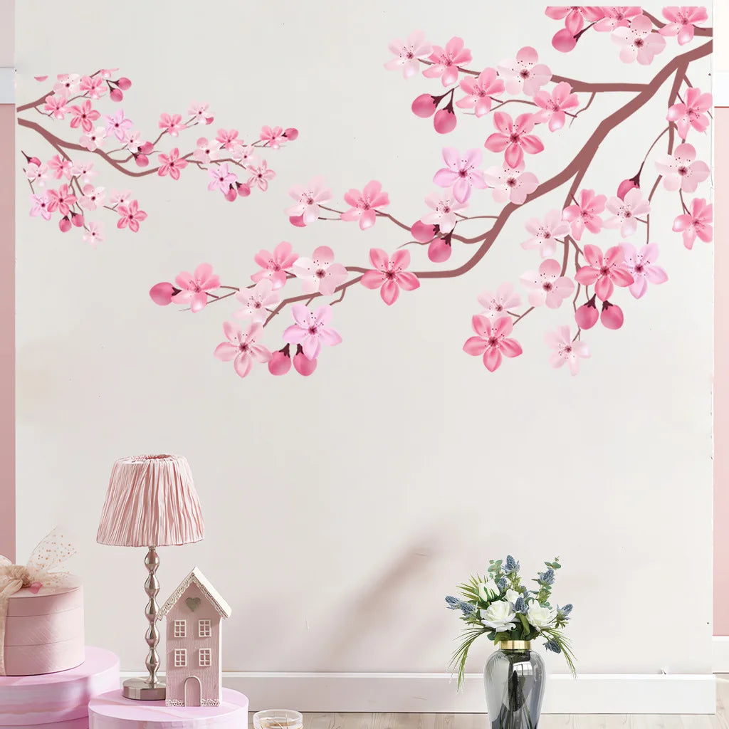 Pink peach blossom branch wall decals featuring pink flowers on a white wall with a small house and floral arrangement.