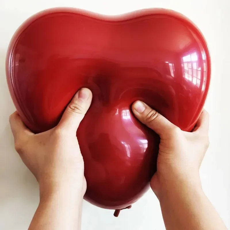 A hand is holding a glossy red heart-shaped latex balloon against a white background.