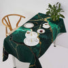 Mantel verde oscuro con textura de mármol dorado, puesto para una comida festiva, con platos y cubiertos blancos.