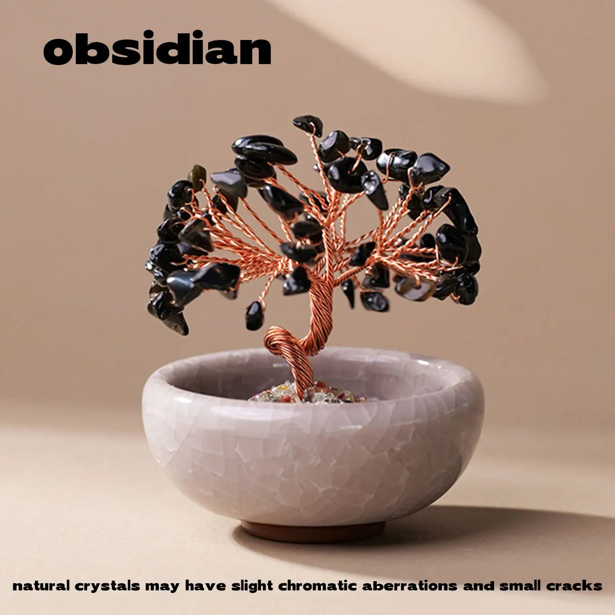 A handcrafted crystal tree with dark stones mounted on a copper wire base sits in a light-colored stone bowl.