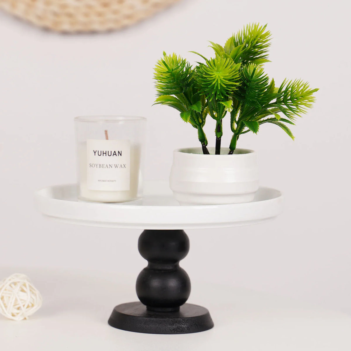 Une bougie blanche et un bonsaï artificiel vert sont présentés sur un socle noir.