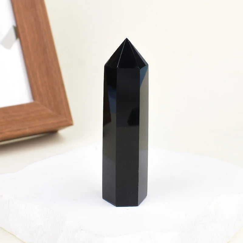 A black natural obsidian crystal obelisk point standing on a white surface.