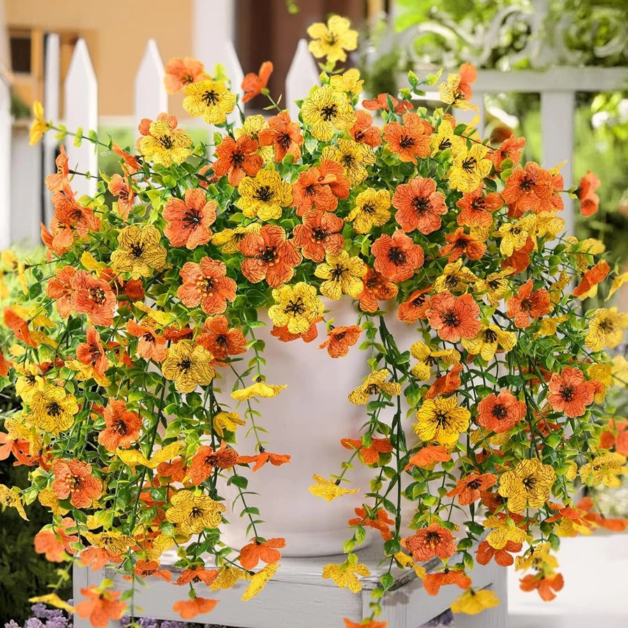 Un arrangement vibrant de vignes de glycine artificielles orange et jaunes décorant un pot blanc.