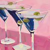 Three martini glasses filled with blue liquid and green olives on pink surfaces