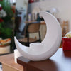 A white, modern moon-shaped decorative vase resting on a wooden surface.