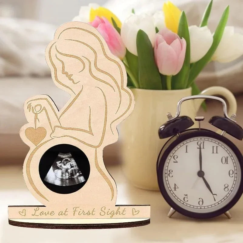 A wooden ultrasound photo frame with a silhouette of a pregnant woman and a vintage alarm clock.