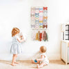 A wall-mounted headband holder for girls with various colored bows displayed on a hanger against a white wall.