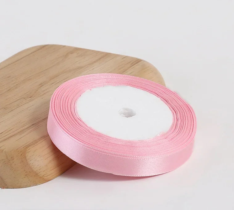 Pink silk satin ribbon rolled on a wooden cutting board.