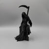 A black figurine of a gothic female grim reaper holding a scythe.