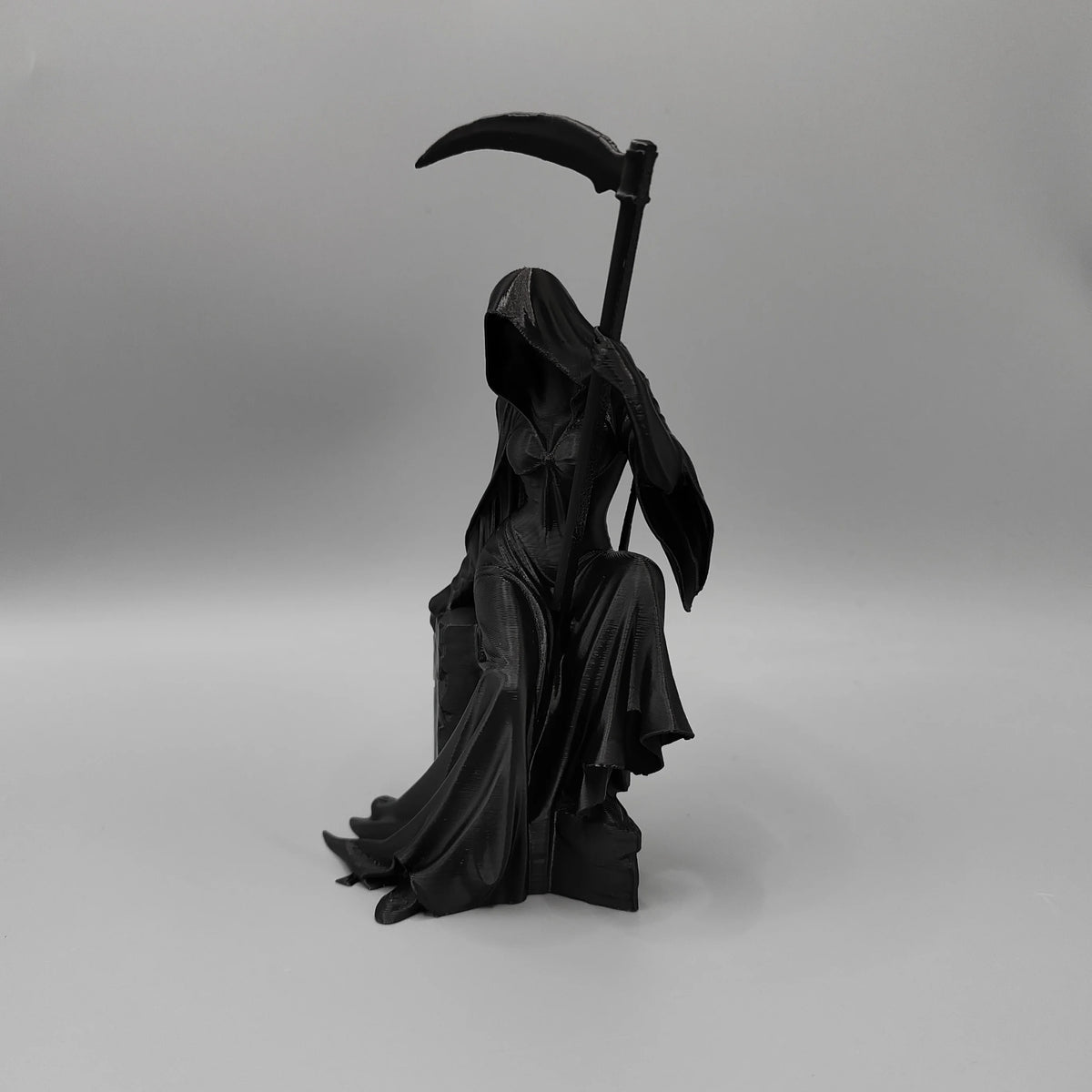A black figurine of a gothic female grim reaper holding a scythe.