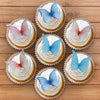 A collection of cupcakes decorated with butterfly toppers in shades of pink, blue, and white on a wooden surface.
