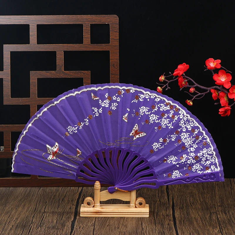 Purple folding fan decorated with white and gold plum blossoms displayed on a wooden stand.