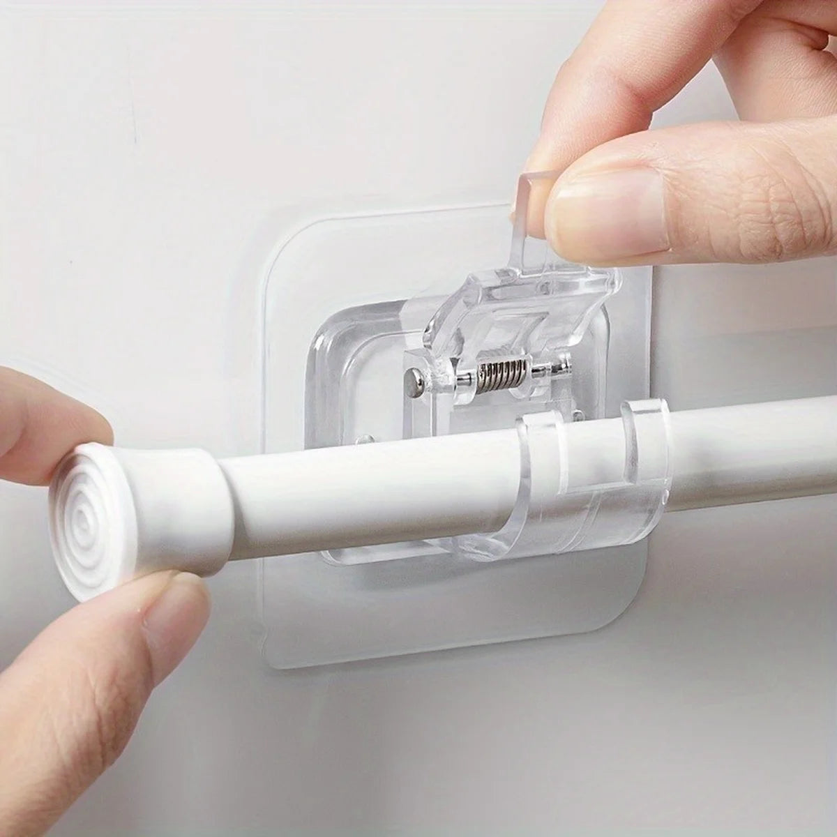 Hands are installing self-adhesive curtain rod holders onto a white wall, showing the clear plastic holder and white rod.