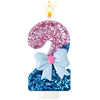 A glittery pink number 9 candle with a blue bow on a white stand, lit by a flame.