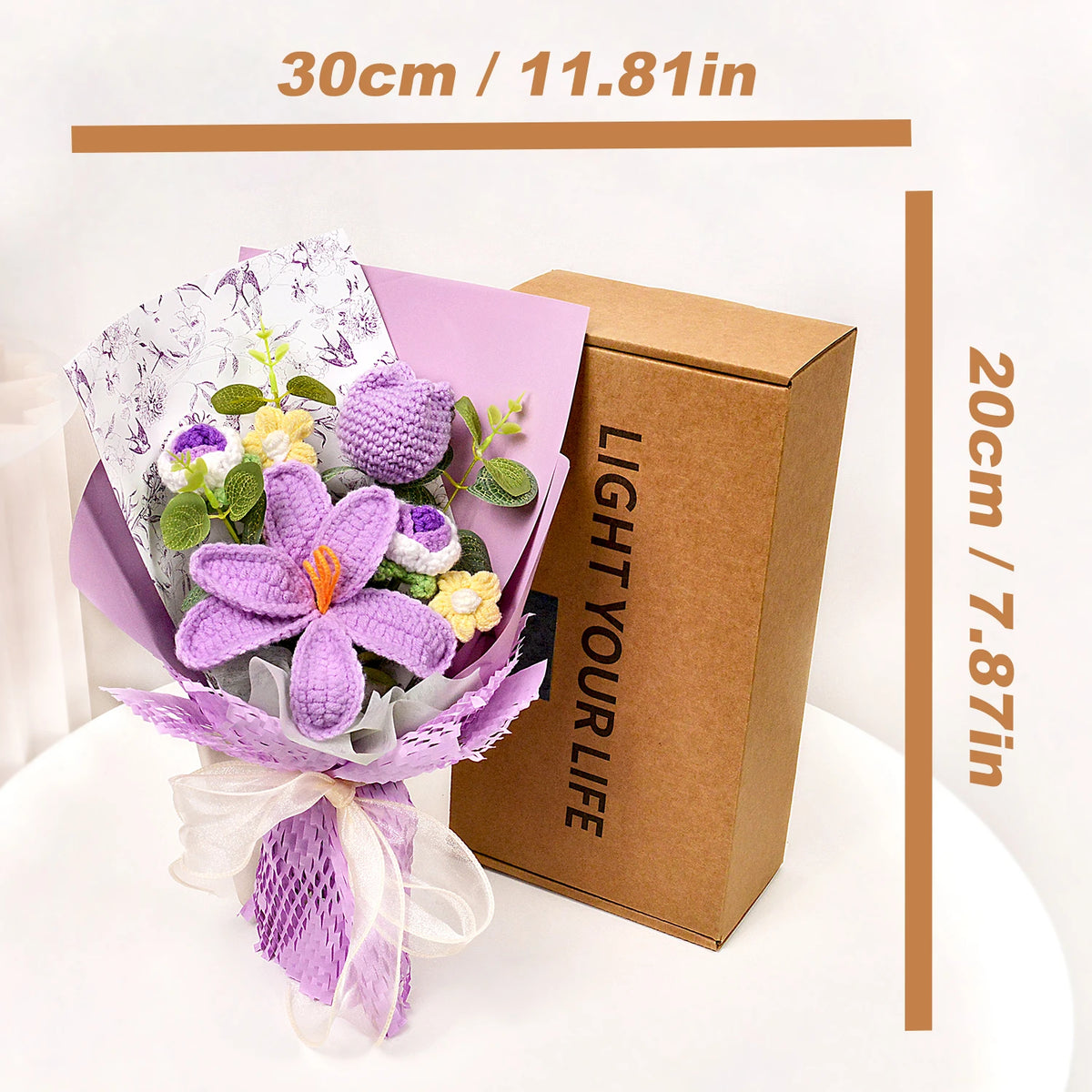 A handmade crochet tulip bouquet in purple and white is displayed next to its brown cardboard box.