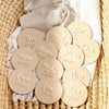 A collection of round wooden milestone cards numbered one through ten, arranged on a woven mat.