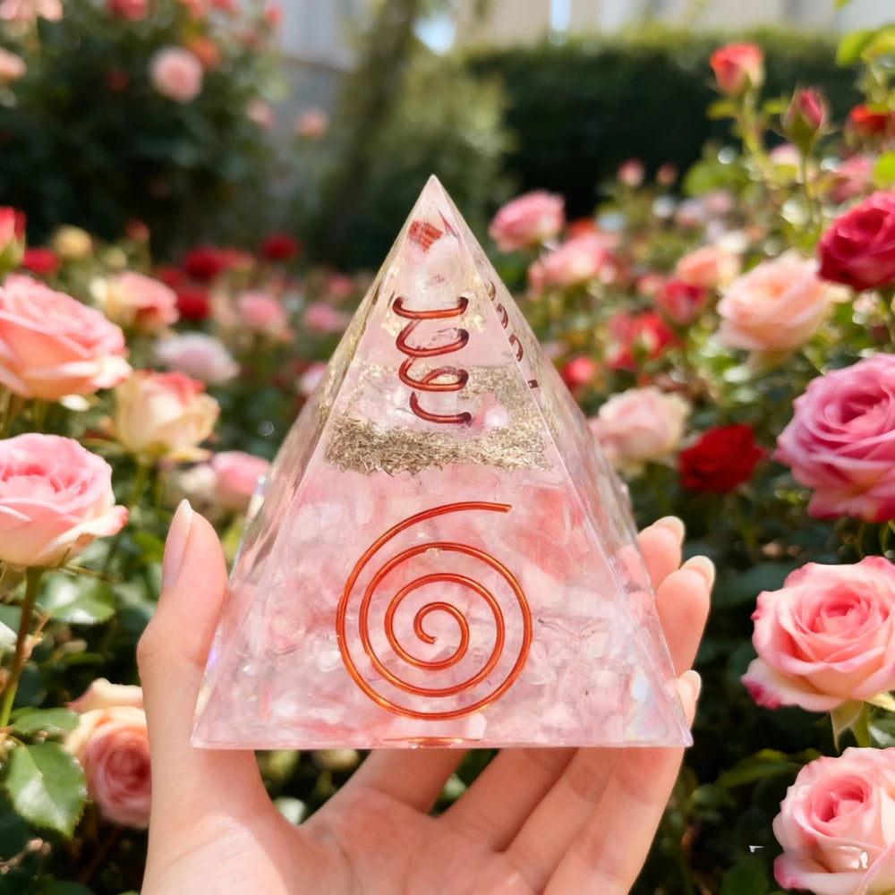A hand holds a pink resin pyramid with natural obsidian and copper coils amidst pink roses.