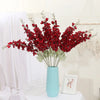Un bouquet de fleurs artificielles de delphinium rouges dans un vase bleu clair, sur une surface blanche.