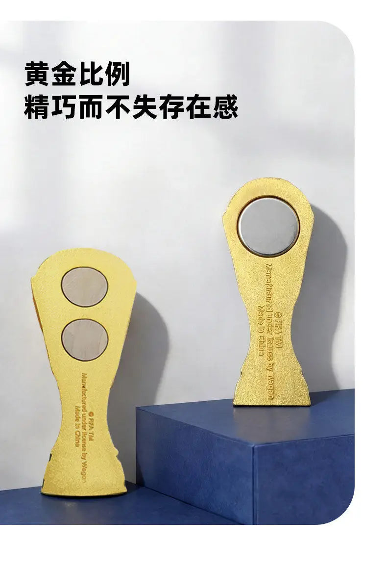 A gold-colored fridge magnet shaped like a soccer trophy, featuring a reflective surface.