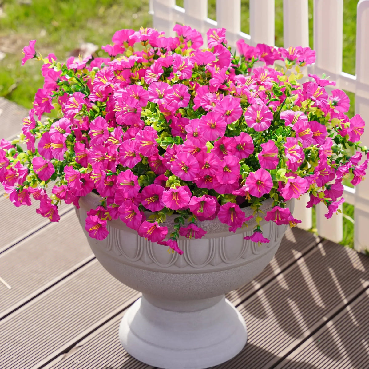 A vibrant pink artificial morning glory and eucalyptus flower arrangement in a gray urn