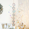 A crystal sunshine catcher set hangs on a white wall next to a decorated white Christmas tree.