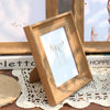 A wooden photo frame with a glass cover displaying vertical brush strokes, resting on a lace cloth.