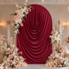 A dramatic red velvet drape serves as an arch cover for a wedding or event backdrop decorated with white and pink floral arra
