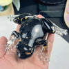 A glossy black crystal frog resin craft decoration with gold flakes is held in a hand.