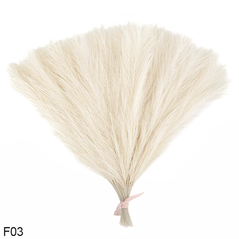 A bundle of light beige artificial pampas grass or reed bouquet with a pink ribbon tied at the bottom.