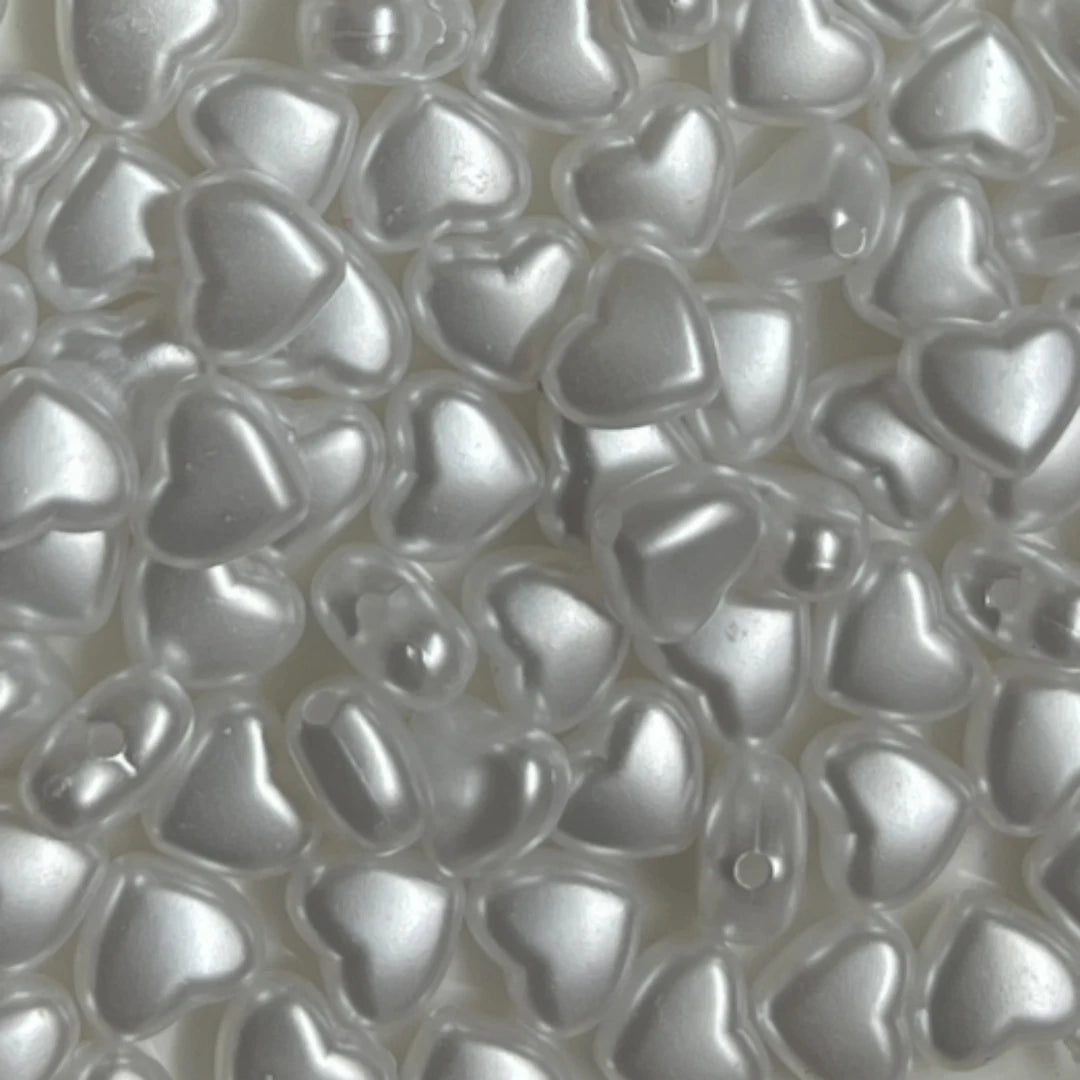 Close-up view of small, heart-shaped acrylic decoration beads in white.