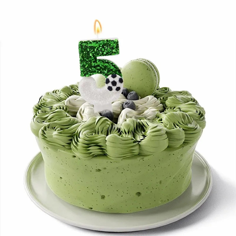 A green frosted cake shaped like the number 5 decorated with soccer-themed elements and a lit candle.
