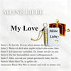 A silver pendant necklace shaped like an open book with a gold clasp and a heart charm, featuring German text.