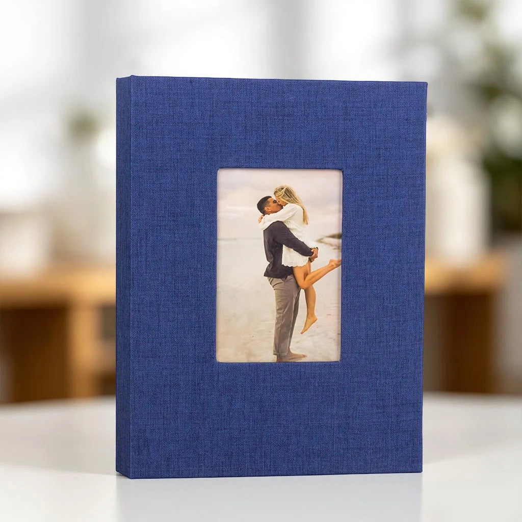 A dark blue linen photo album with a front display window showing a couple embracing against a light background.