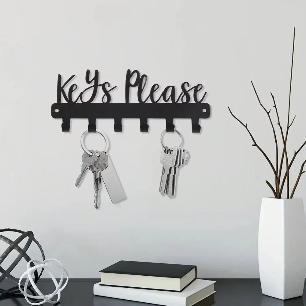 Black wall-mounted metal key holder with hooks displaying keys on a gray wall.