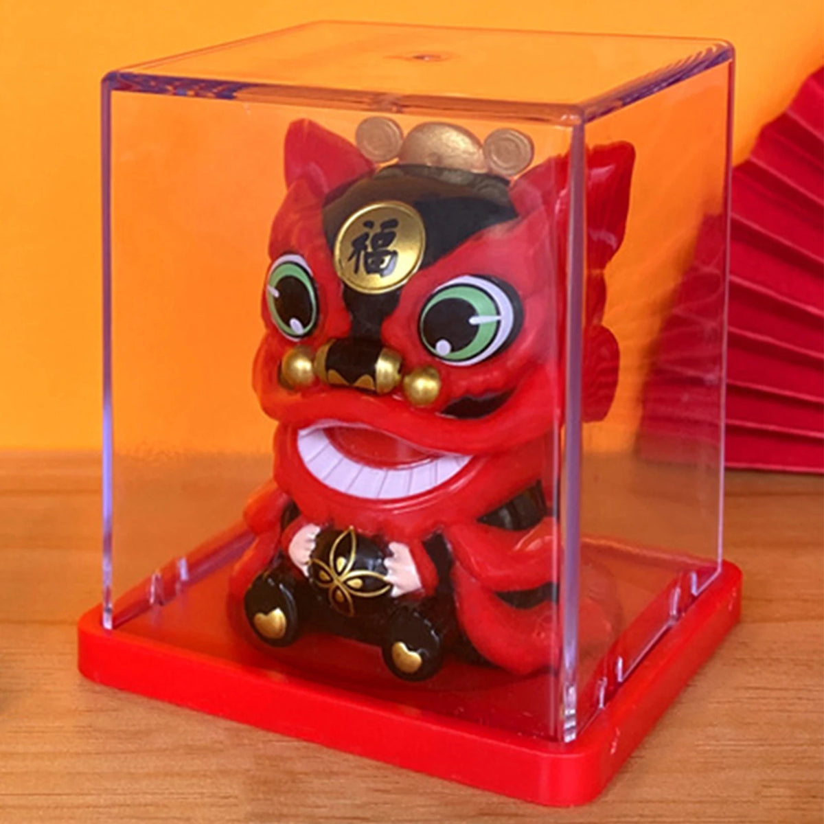 A red solar-powered figurine of a waving lucky cat with large eyes and a golden crown displayed in a clear box.