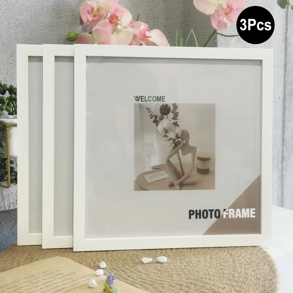 A set of three white photo frames displayed on a light-colored surface with floral decorations.