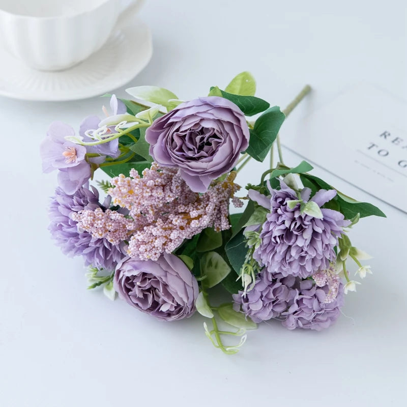 A bouquet of artificial silk peony flowers in shades of lavender and purple on a white surface.