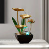 A golden lotus pond tabletop water fountain with green leaves and blue LED lighting in a black pot.