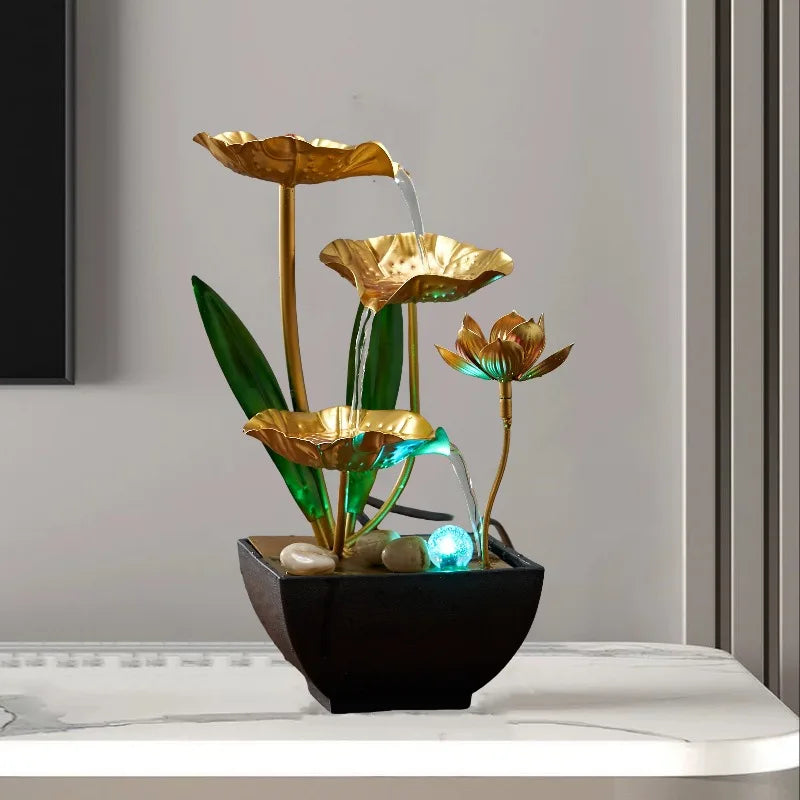 A golden lotus pond tabletop water fountain with green leaves and blue LED lighting in a black pot.