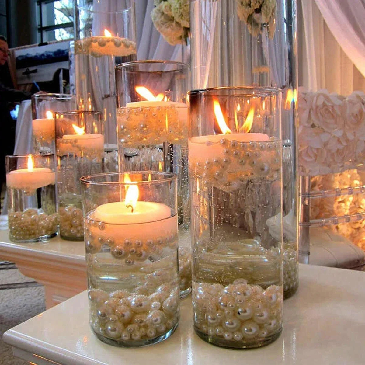 Clear glass candle holders filled with pearls and candles arranged on a white surface.