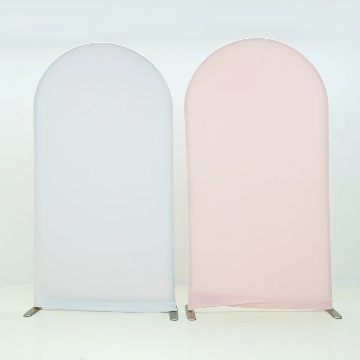 A pair of stretchable arch backdrop covers, one white and one blush pink, displayed against a light background.