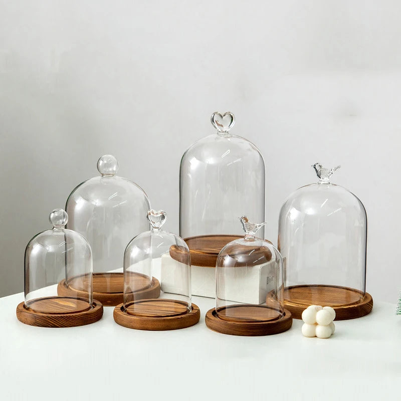 Clear glass aromatherapy candle holders with wooden bases and decorative lids arranged on a white surface.