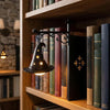 A dark metal witch hat lamp illuminates a row of old books on a wooden shelf.