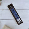 A package of long thin blue birthday candles with white tips displayed on a white wooden surface.