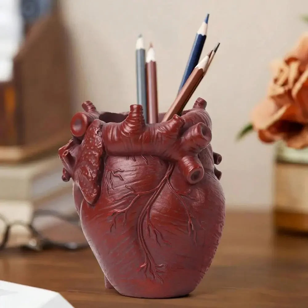 A reddish-brown heart-shaped resin pen organizer filled with colored pencils and pens on a wooden desk.