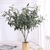 Artificial olive branch with dark green leaves and small fruits displayed in a glass vase.