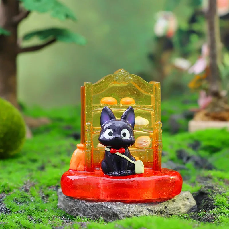 A black cat figurine in a glass display sits on a red base surrounded by green moss and rocks.