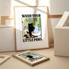 A framed poster titled Wash Your Little Paws featuring a black cat in a bathtub surrounded by colorful bathroom elements.
