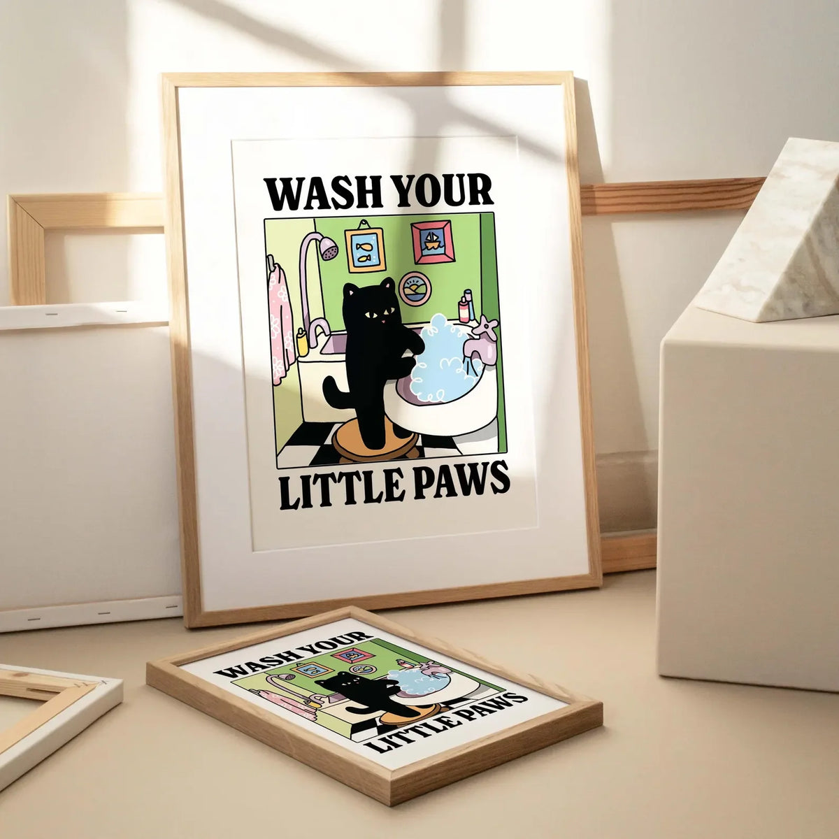 A framed poster titled Wash Your Little Paws featuring a black cat in a bathtub surrounded by colorful bathroom elements.
