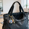 A dark gray fabric bag with a gold-colored FIFA trophy keychain attached to the zipper pull.